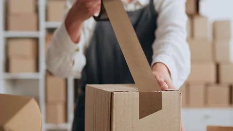 Packing a box A parcel warehouse worker packs a box with brown tape, Packing Stock Footage 219864751