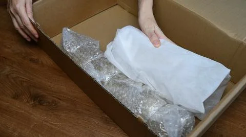 Packing up fragile tableware into plastic bubble wrapping inside cardboard box Stock Photos