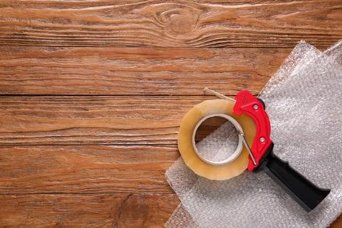 Packing tape dispenser with bubble wrap on wooden table, shipping and moving  Stock Photos