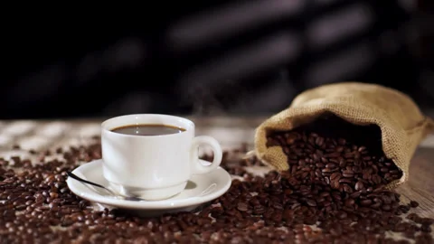 Packshot of White Coffee Cup with Hot Steam and Coffee Beans Around Stock Footage 303519157