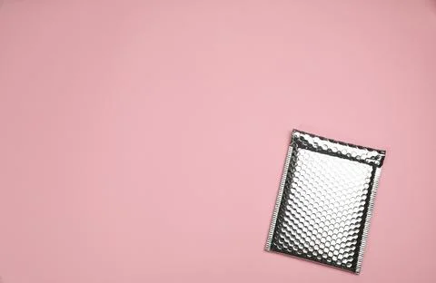 Padded envelope with bubble wrap on light pink background, top view. Space fo Stock Photos