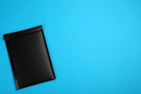 Padded envelope with bubble wrap on light blue background, top view. Space fo Stock Photos