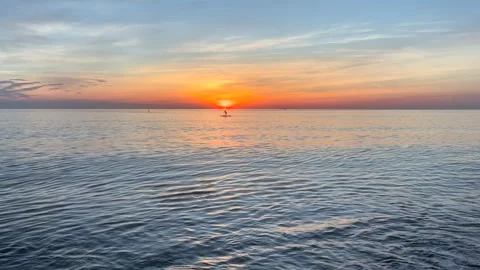 Paddle boarder gliding across calm sea directly beneath rising sun. Golden Stock Footage 337777134