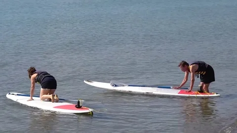 PADDLE BOARDERS (2 THEN A THIRD) GET ON THEIR BOARDS AND PADDLE OUT Stock Footage 79363279