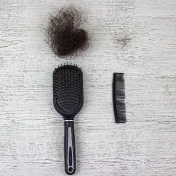 A paddle brush, a comb and two clumps of hair on a wooden background. Stock Photos