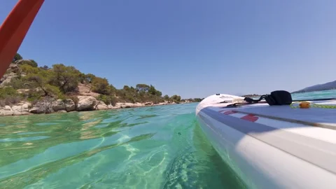 Paddleboard gliding through crystal-clear turquoise water near a rocky coastline Stock Footage 313803066