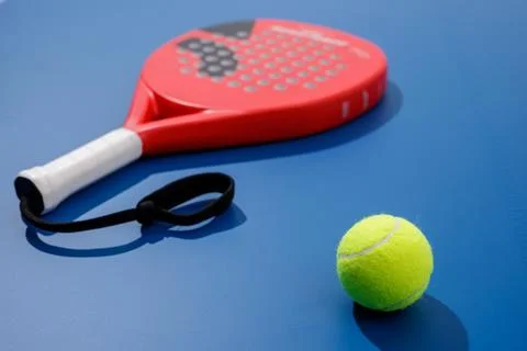 Padel ball in focus with blurred racket on blue court background copy space Stock Photos