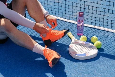 Padel player tying shoelaces before training on an outdoor court Stock Photos