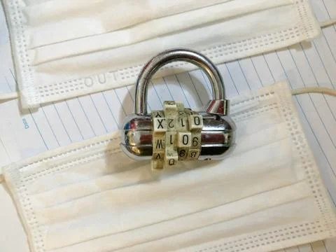 Padlock combination lock on white surgical medical masks for lockdown like Stock Photos