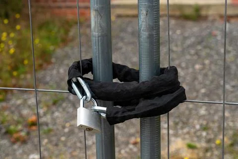 Padlock securing a chain around two metal posts by a fence Stock Photos