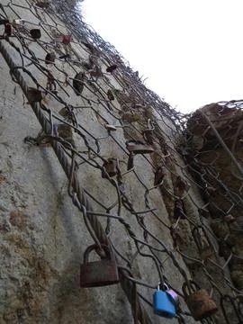 Padlocks on wire mesh over rugged stone wall, low angle close against brigh.. 库存照片