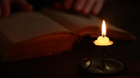 Page of old book being turned over by man hand with burning wax candle at night Stock Footage 304448049