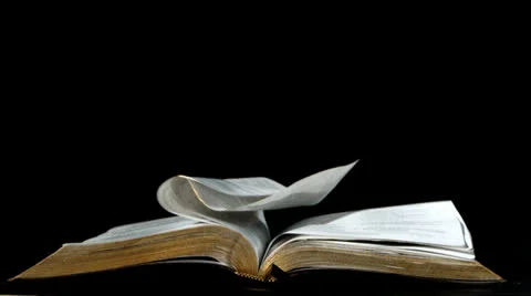 Pages of the bible turning in the wind on black background Stock Footage