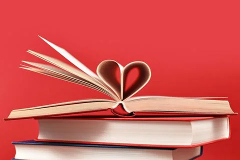 Pages folded into heart shape on stack of old hardcover books on red background Stock Photos