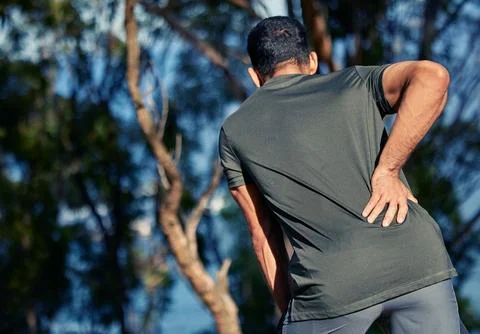 This pain will affect my form. Rearview shot of a sporty young man holding his Stock Photos