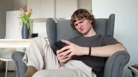 With a pained expression, the young man holds his phone and covers his face with Stock Footage 302634386