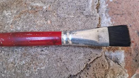 Paint brush with red handle on textured surface. Artist tool for creative Stock Photos