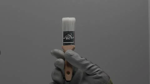 A paint brush rotates in a hand on a gray background. Stockbeeldmateriaal 266495773