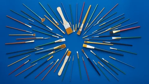 Paint brushes in circular burst pattern. Flat lay shot, blue background. 4k loop Video stock 125535686
