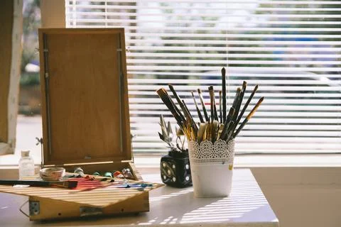 Paint brushes, paint box and art supplies arranged on a table in a bright a.. Stock Photos