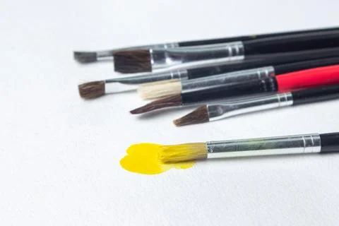 Paint brushes on a white background. One brush with yellow paint.  Stock Photos