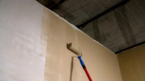 Paint roller applying beige paint to wall under exposed ceiling grid Stock Photos
