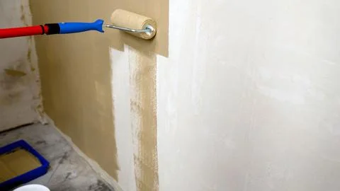 Paint roller applying beige paint to interior wall, blue tray and red handl.. Stock Photos