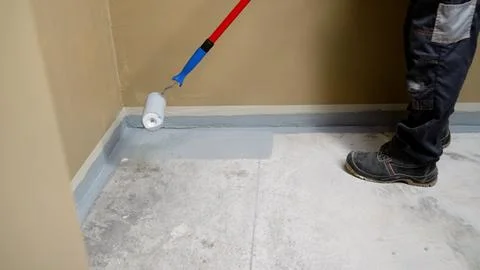 Paint roller applying gray paint to concrete floor near wall base Stock Photos