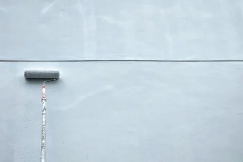 Paint Roller Applying Light Grey Paint on Grunge Wall. Stock Photos