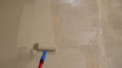 Paint roller applying white paint on beige wall during interior renovation Stock Footage 338385405