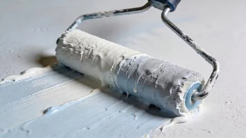 Paint roller applying white paint on wall surface. Close-up of home renovation p Stock Photos
