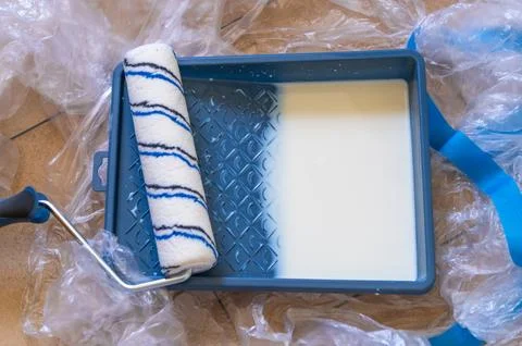 Paint roller loaded with white paint resting on plastic drop cloth Photos