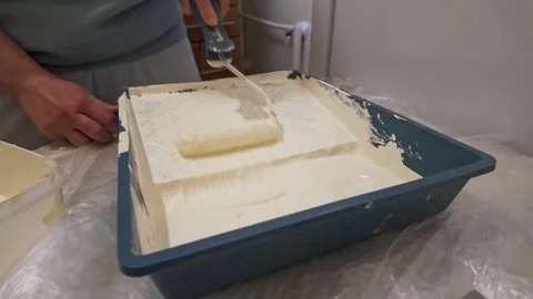 Paint roller loading with white paint in tray on protected table Stock Footage 335314999