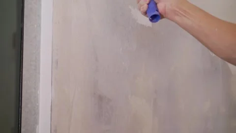 A paint roller with a long handle applies primer to a raw plasterboard wall d. Stock Footage 331512495