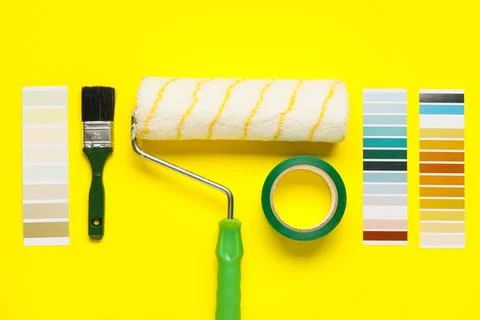 Paint roller with palette samples, brush and adhesive tape roll on yellow bac Stock-Fotos