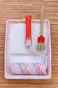 Paint roller with a red handle and a pink plastic paint tray on floor. Stock Photos