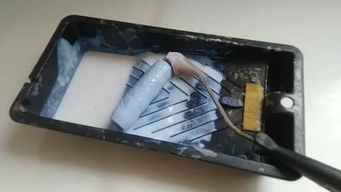 A paint roller rests in a dark tray with white paint, showing an active home  Stock Photos