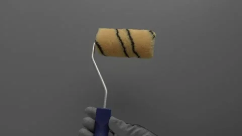 A paint roller rotates in a hand on a gray background. 스톡 동영상 266981581