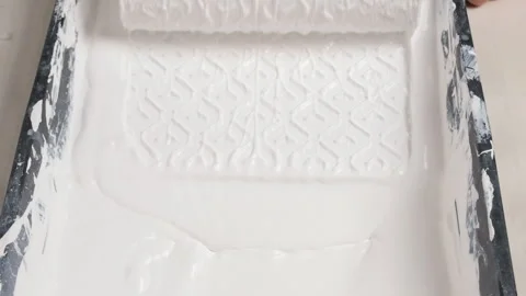 Paint roller soaked in thick white paint inside a textured tray. Close up Stock Footage 311051856