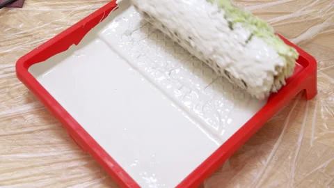 Paint roller soaking in white paint tray on floor Stock Footage 321663851