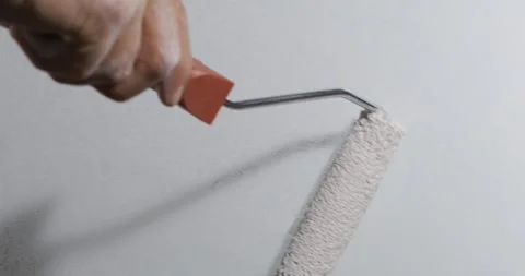 Paint roller spreads light coat across gray wall as hand guides each pass. .. Stock Footage 348442444