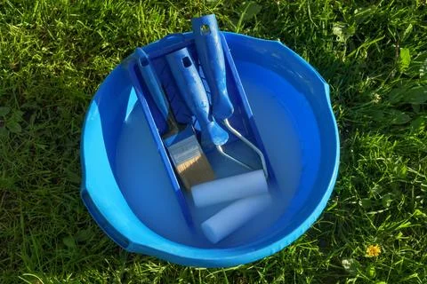 Paint rollers and brush rest in blue basin with soapy water on green grass, Stock Photos