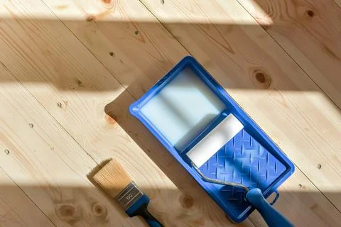 Paint tray with roller and brush on spotless wooden floor embodies preparatio Stock Photos