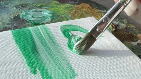 A paintbrush applying green paint on a textured canvas surface. 스톡 동영상 343300859