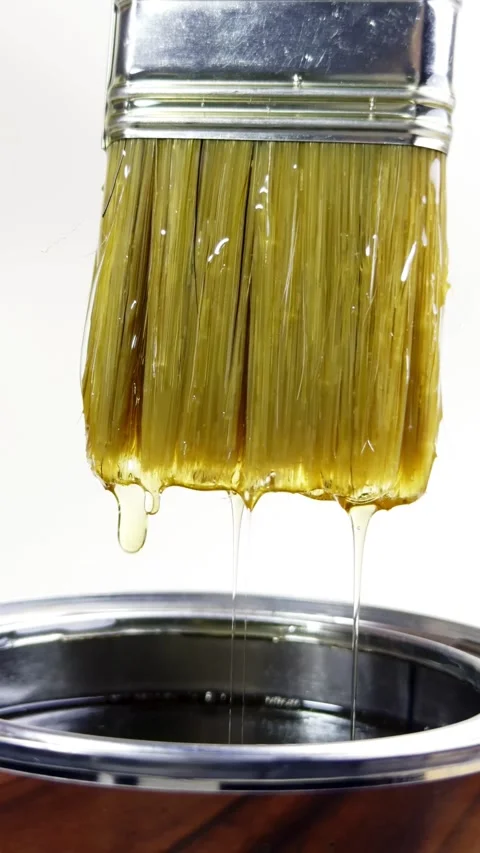 Paintbrush dripping with thick yellow liquid into metal pot Video stock 331774282