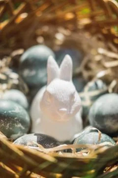 Painted blue textured easter eggs and a white plastic rabbit in a wicker brown Stock Photos
