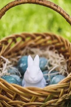 Painted blue textured easter eggs and a white plastic rabbit in a wicker brown Stock Photos