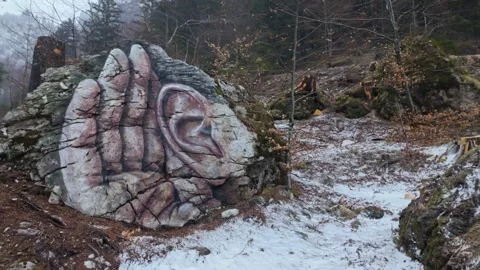 Painted boulder with facial elements stands on a snowy forest trail in Sorica Stock Footage 337507731