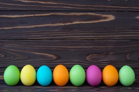 Painted colorful Easter eggs on dark wooden boards. Paschal template with tex Stock Photos
