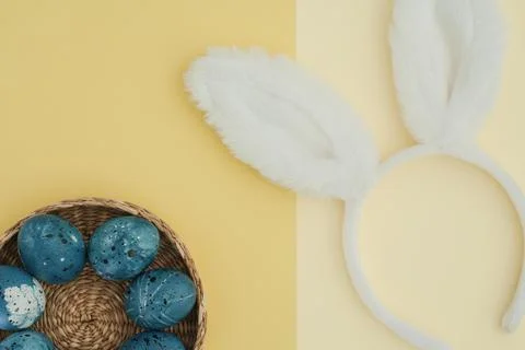 Painted Easter eggs in a basket and bunny ears on a yellow trendy background Stock Photos